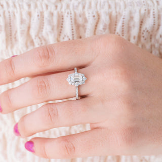 White gold engagement ring set with emerald cut diamond center stone and accents on hand over a light background 