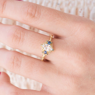 Yellow gold engagement ring with oval cut diamond center stone and lab-grown alexandrite accents on hand over a light background 