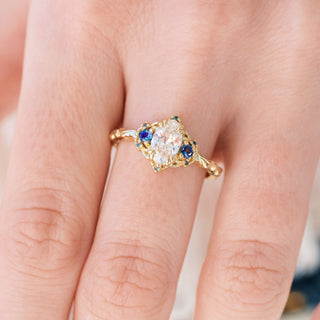 Yellow gold engagement ring with oval cut diamond center stone and lab-grown alexandrite accents on hand over a light background 