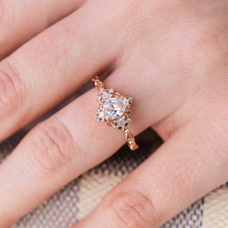 Rose gold engagement ring with oval cut diamond center stone and diamond accents on hand over a light background 