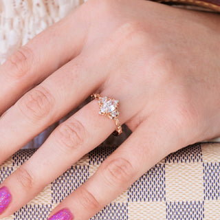 Rose gold engagement ring with oval cut diamond center stone and diamond accents on hand over a light background 