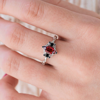 White gold engagement ring with oval cut lab-grown ruby center stone and black onyx accents on hand over a light background 