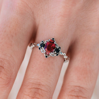 White gold engagement ring with oval cut lab-grown ruby center stone and black onyx accents on hand over a light background 