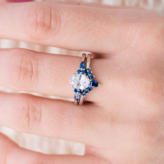 White gold engagement ring set with oval cut diamond center stone and lab-grown blue sapphire accents on hand over light background