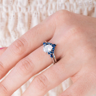 White gold engagement ring set with oval cut diamond center stone and lab-grown blue sapphire accents on hand over light background