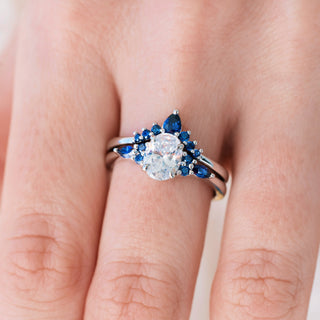 White gold engagement ring set with oval cut diamond center stone and lab-grown blue sapphire accents on hand over light background