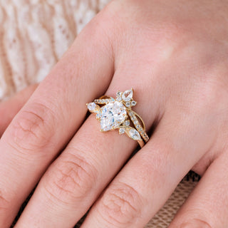 Yellow gold engagement ring set with teardrop diamond center stone and accents on hand over light background