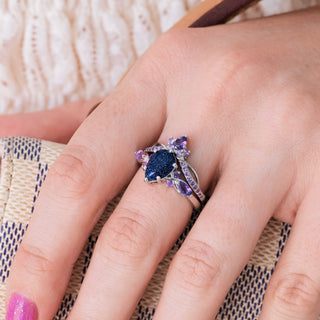 White gold engagement ring set with teardrop blue sandstone center stone and natural amethyst accents on hand 