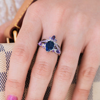 White gold engagement ring set with teardrop blue sandstone center stone and natural amethyst accents on hand 