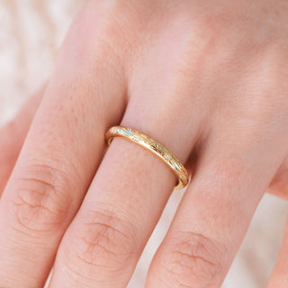 Yellow gold 2mm wedding band with floral design on hand over a light background 