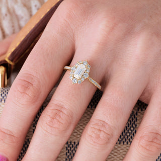 Yellow gold engagement ring set with emerald cut diamond center stone and accents on hand over a light background 