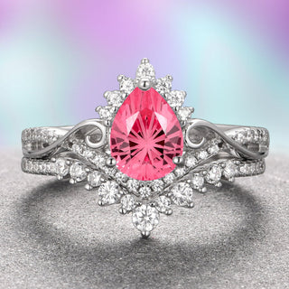 A fantasy cut pink sapphire engagement ring set in 14K white gold, with Moissanite accent stones on the band, displayed against a gradient purple and pink background.
