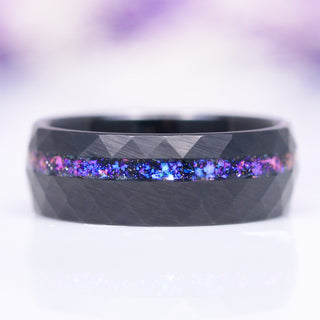 An 8mm black hammered tungsten wedding band with an inlay of crushed fire opal and galaxy sandstone, displaying a contemporary, masculine aesthetic.