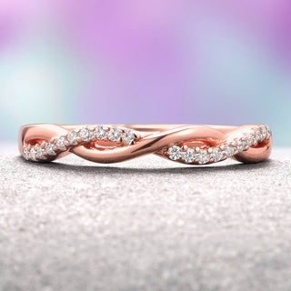 A rose gold wedding band with twisted design and embedded diamonds, displayed against a gradient purple background.