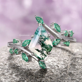 A sterling silver ring featuring a kite-shaped moss agate stone with green patterns, accented by smaller green emerald stones, displayed against a purple background.