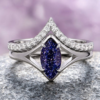 A sterling silver engagement ring set featuring a marquise cut blue sandstone center stone with chevron band design and smaller clear accent stones, displayed against a purple background.