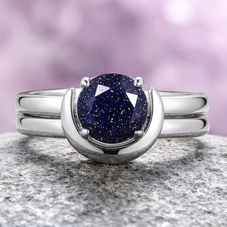 An engagement ring set featuring a crescent moon design with a blue starry center stone, placed on a rock surface.