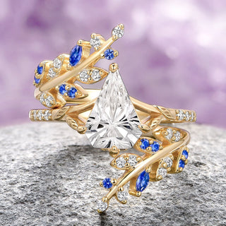 An 18k solid yellow gold ring set featuring a central alexandrite stone with leaf patterns, surrounded by emerald and cubic zirconia stones on a textured background.