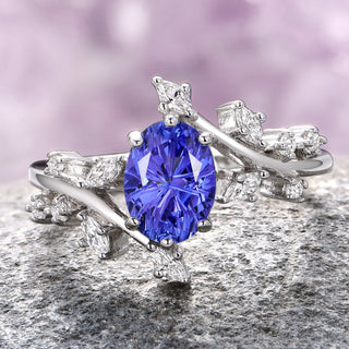 An oval-cut purple sapphire ring with a fairy leaf design, crafted in 14K white gold, displayed against a textured background.