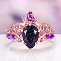 Feyra Starry Night & Amethyst Couples Ring Set featuring a pear-shaped dark blue sandstone center stone surrounded by vibrant amethyst gemstones set in a delicate rose gold band, crafted by Aquamarise for Matching Couples' Rings and February Birthstone collections.