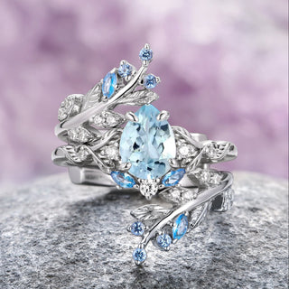 A two-piece 14K white gold ring set featuring a large pear-cut natural aquamarine with leaf motifs, set on a rock against a purple background.