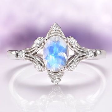 Maeve Vintage Moonstone Engagement Ring in 14K White Gold featuring an oval moonstone with ethereal blue flashes, surrounded by delicate white gold filigree and small sparkling diamond accents, crafted by Aquamarise Gold.