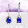 Vera Teardrop Sapphire Dangle Earrings in Sterling Silver featuring royal blue teardrop sapphires surrounded by sparkling accents on elegant silver hooks by Aquamarise.