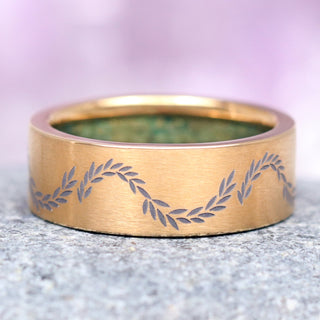 An 8mm gold titanium men's wedding band featuring leaf patterns and a hidden moss agate inlay visible only from the inside of the ring.