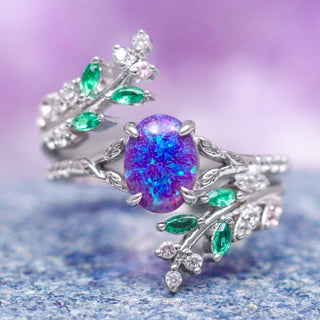 A sterling silver ring with a central lavender opal surrounded by green leaf-shaped accent stones, set against a purple background.
