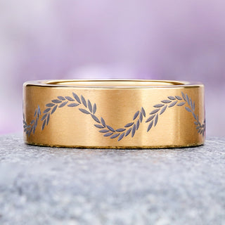 Laurel etched gold titanium wedding band on granite, showing the gray leaves around the 8mm flat brushed band