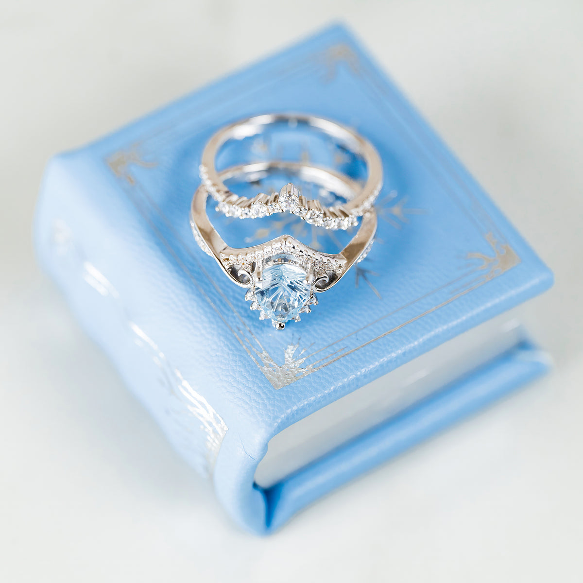 Winter Court Leather Book Ring Box – Frost Sky Edition (Small) by Aquamarise featuring elegant silver rings on a light blue leather book box with gold detailing, perfect for meaningful jewelry gifts.