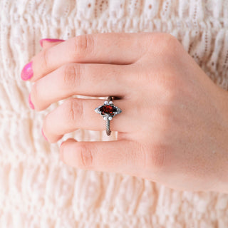 Hand wearing a ring with a red gemstone on a textured beige background
