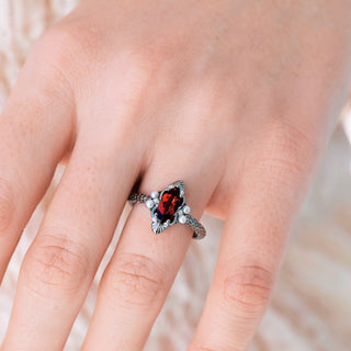 Silver ring with a red gemstone on a person's finger against a blurred background