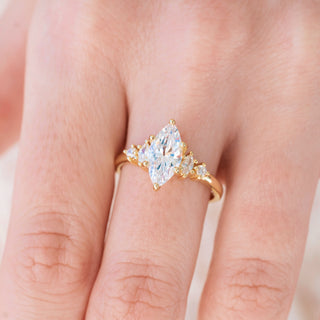 Yellow gold ring with marquise cut diamond center stone and accents on hand over light background 