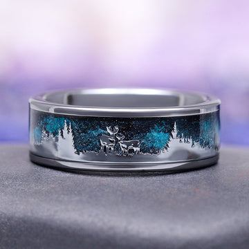 Silver ring with engraved design of deer in a forest on a gray surface with a blurred purple background