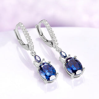 Blue Moissanite Earrings Midnight Blue Drop Earrings over a light purple background 
