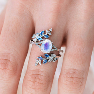 White gold ring set with oval cut natural rainbow moonstone center stone and aquamarine accents on hand over a light background