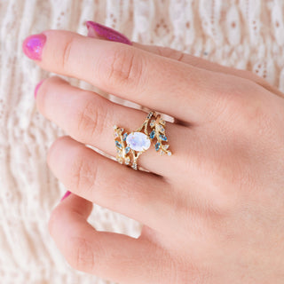 Yellow gold ring set with oval cut natural rainbow moonstone center stone and aquamarine accents on hand over a light background