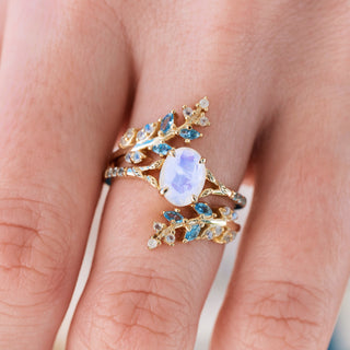 Yellow gold ring set with oval cut natural rainbow moonstone center stone and aquamarine accents on hand over a light background