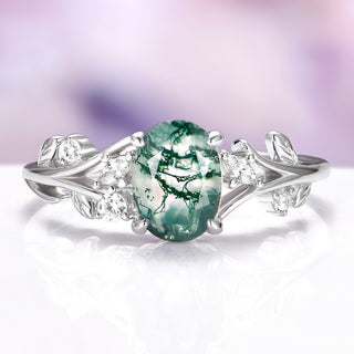 Moss agate engagement ring with leaf design and diamond accent stones over light purple background