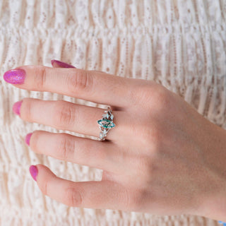 Hand wearing a silver ring with a green gemstone on a textured beige background