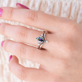 Silver ring with a colorful gemstone on a hand against a neutral background