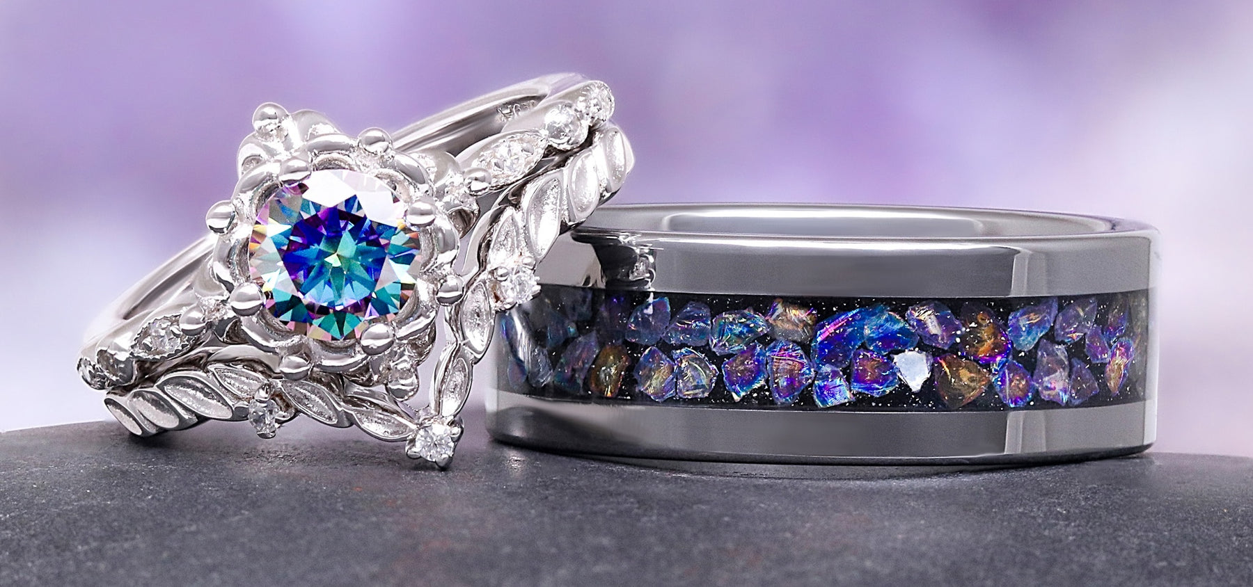 Two rings with colorful gemstones on a gray surface with a purple gradient background