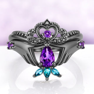 Natural Amethyst Claddagh Engagement Ring Set in Black Ruthenium by Aquamarise, two hands holding a pear amethyst with the heart and crown band nested above