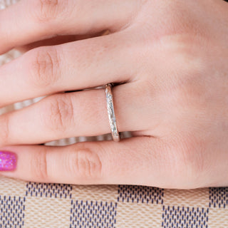 White gold 2mm wedding band with floral design on hand over a light background 