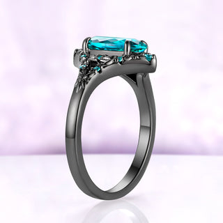 Side profile of the Nerida Paraiba blue spinel ring in black ruthenium, the oval stone held in four prongs above the carved gallery