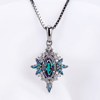 Nightbriar lab-grown alexandrite pendant on its box chain against white satin, showing the teal marquise center and starburst frame