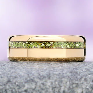 Crushed peridot gold tungsten wedding band on granite, showing the olive-green flakes against the mirror-polished gold