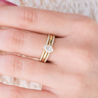 Yellow gold engagement ring set with oval cut diamond center stone and accents on hand over a light background 