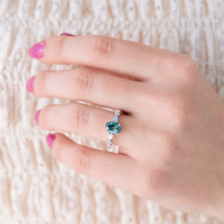 Hand wearing a silver ring with a blue gemstone on a textured white background
